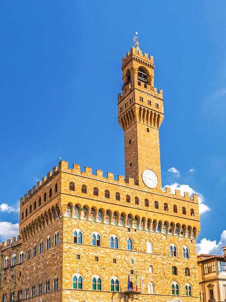 Palazzo Vecchio exterior with clock tower under clear blue sky in Florence, Italy.