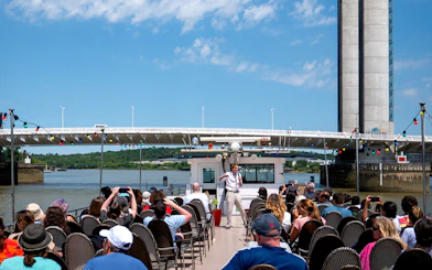 Guide giving live commentary on Bordeaux river cruise with bridge in background.