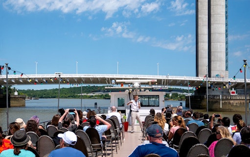 Guide giving live commentary on Bordeaux river cruise with bridge in background.