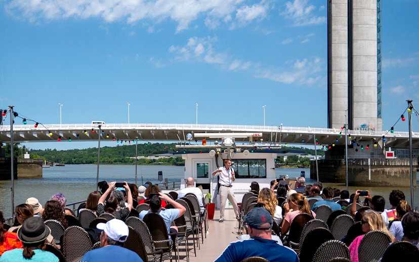 Guide giving live commentary on Bordeaux river cruise with bridge in background.