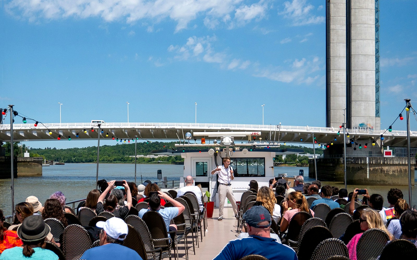 Guide giving live commentary on Bordeaux river cruise with bridge in background.