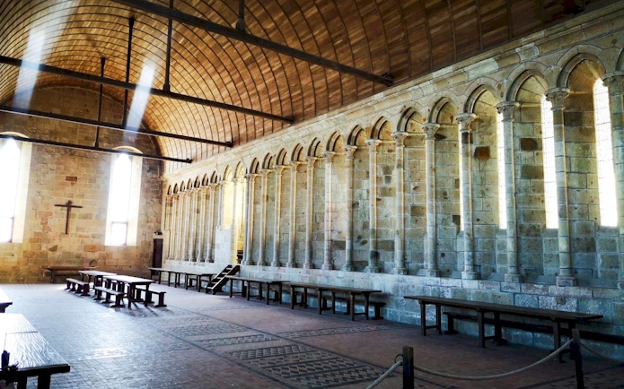 Mont-Saint-Michel Abbey interior with arched columns and wooden benches.