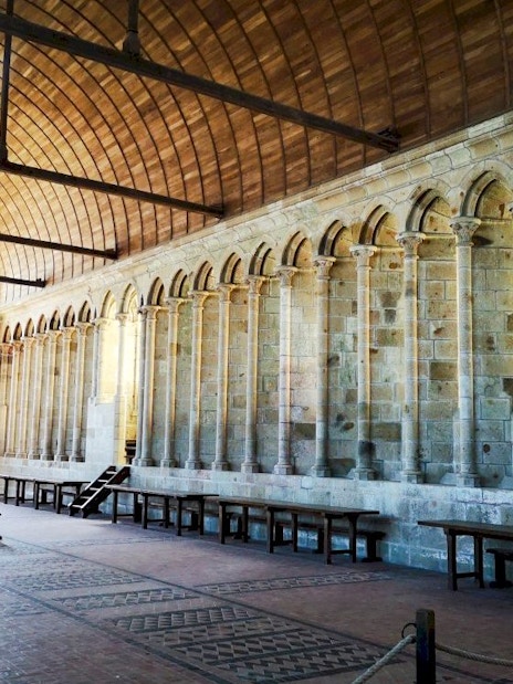 Mont-Saint-Michel Abbey interior with arched columns and wooden benches.