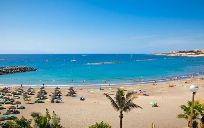 Beach view in Tenerife with sunbathers and umbrellas, ideal for a submarine tour experience.