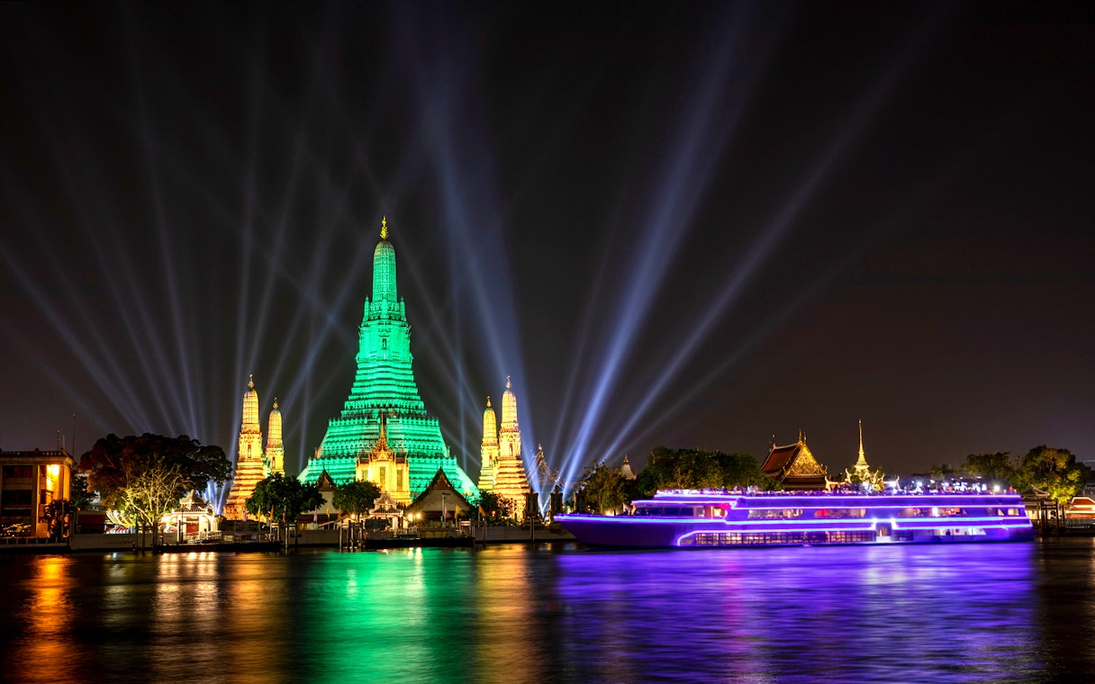 White Orchid River Cruise passing Wat Arun illuminated at night in Bangkok, Thailand.