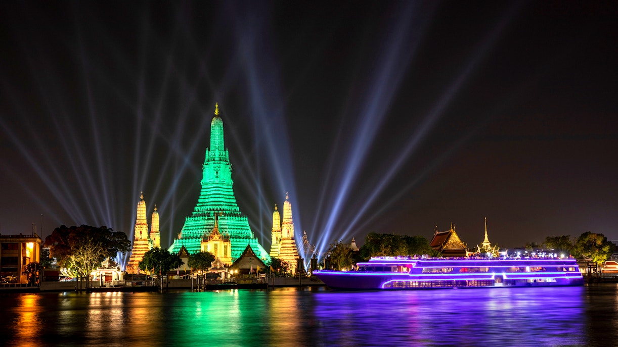 White Orchid River Cruise passing Wat Arun illuminated at night in Bangkok, Thailand.