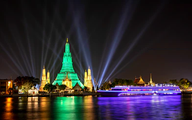 White Orchid River Cruise passing Wat Arun illuminated at night in Bangkok, Thailand.