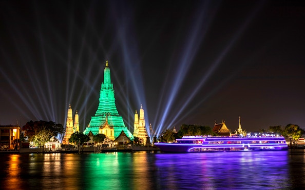 White Orchid River Cruise passing Wat Arun illuminated at night in Bangkok, Thailand.