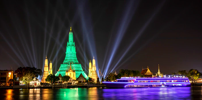 White Orchid River Cruise passing Wat Arun illuminated at night in Bangkok, Thailand.