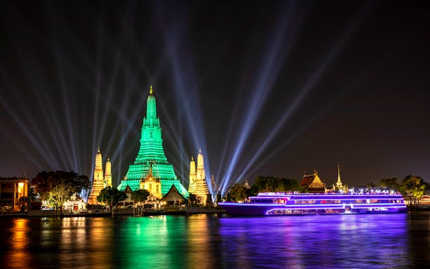 White Orchid River Cruise passing Wat Arun illuminated at night in Bangkok, Thailand.