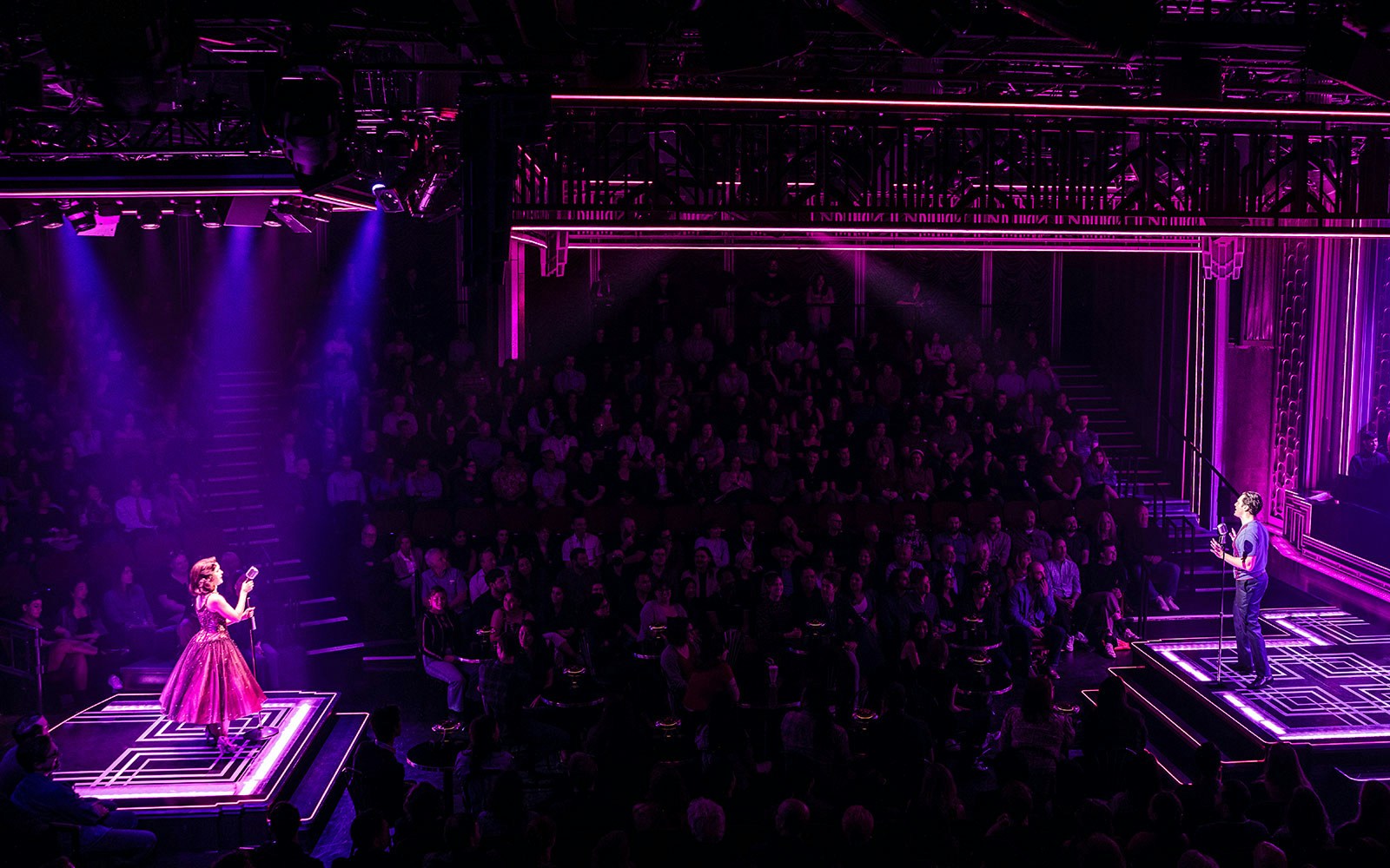 Theater performance with two actors on stage under purple lighting, audience watching.