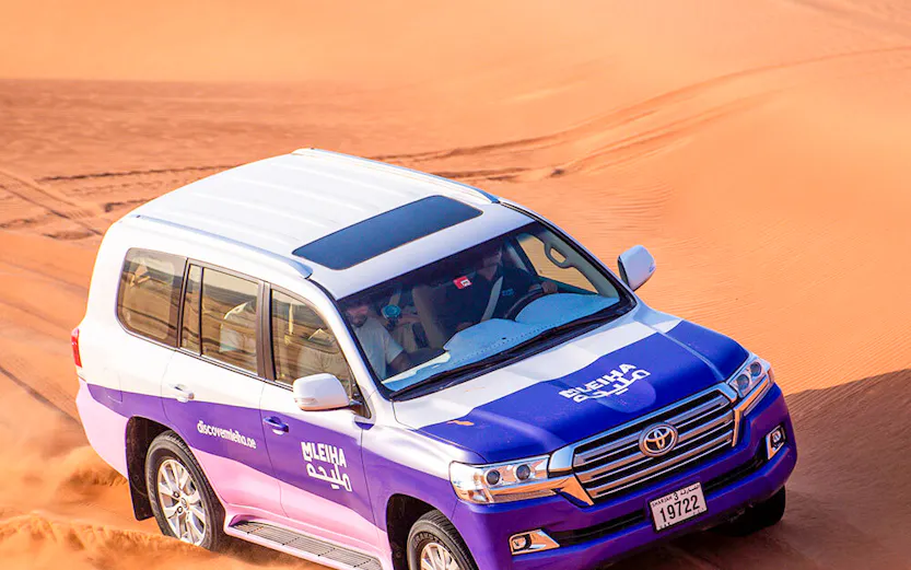 SUV driving through Mleiha desert dunes in adventure tour.
