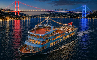 Bosphorus dinner cruise ship with Turkish flag under illuminated bridge, Istanbul.