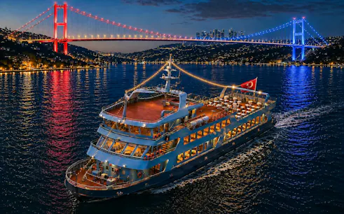 Bosphorus dinner cruise ship with Turkish flag under illuminated bridge, Istanbul.