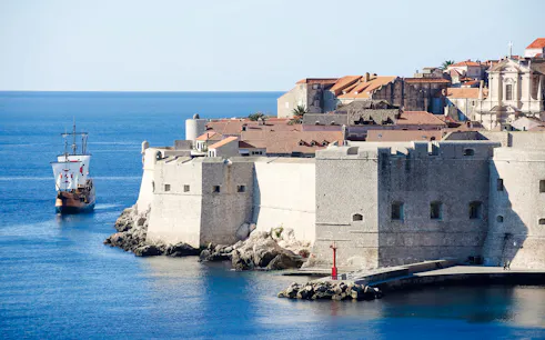 Pirate ship approaching Old Town Dubrovnik's historic walls on a panoramic cruise.
