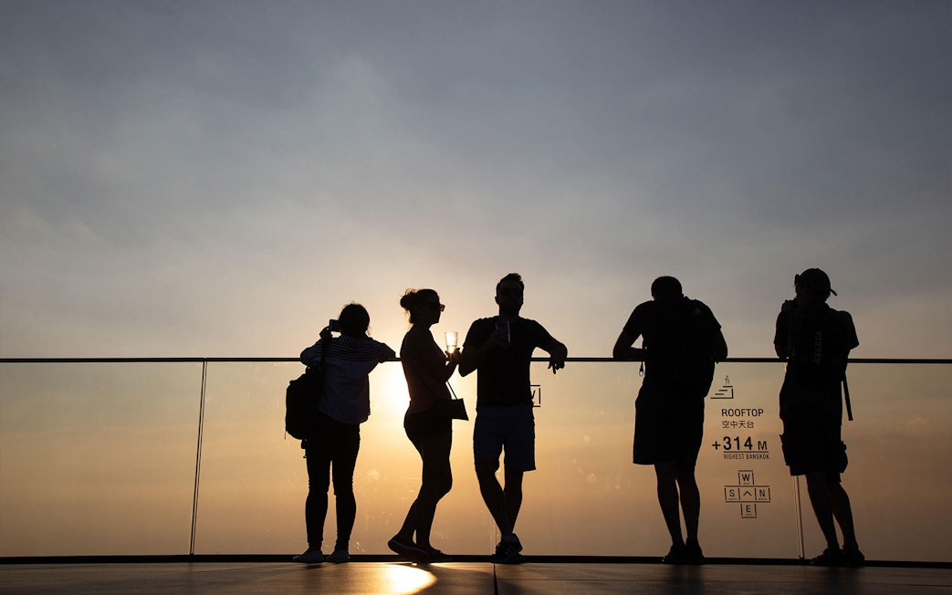 Silhouettes of people enjoying sunset views at Mahanakhon SkyWalk, Bangkok.