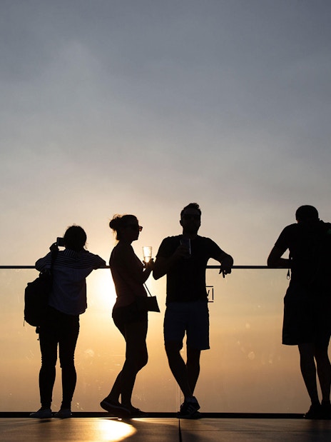 Silhouettes of people enjoying sunset views at Mahanakhon SkyWalk, Bangkok.