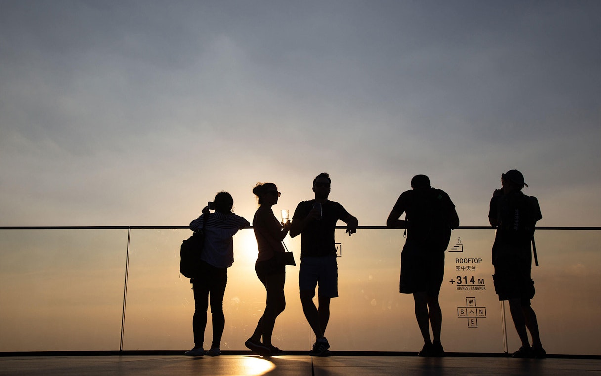 Silhouettes of people enjoying sunset views at Mahanakhon SkyWalk, Bangkok.