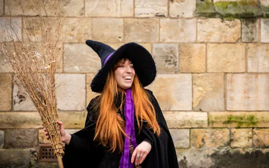 Tour guide in witch costume holding broom on York Witches & History Old Town Walking Tour.