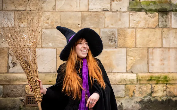 Tour guide in witch costume holding broom on York Witches & History Old Town Walking Tour.