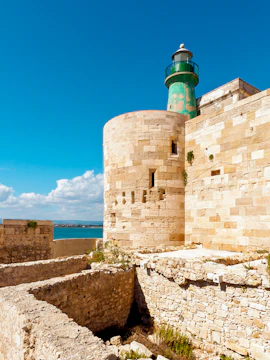 Castello Maniace stone tower and lighthouse against blue sky in Syracuse, Italy.