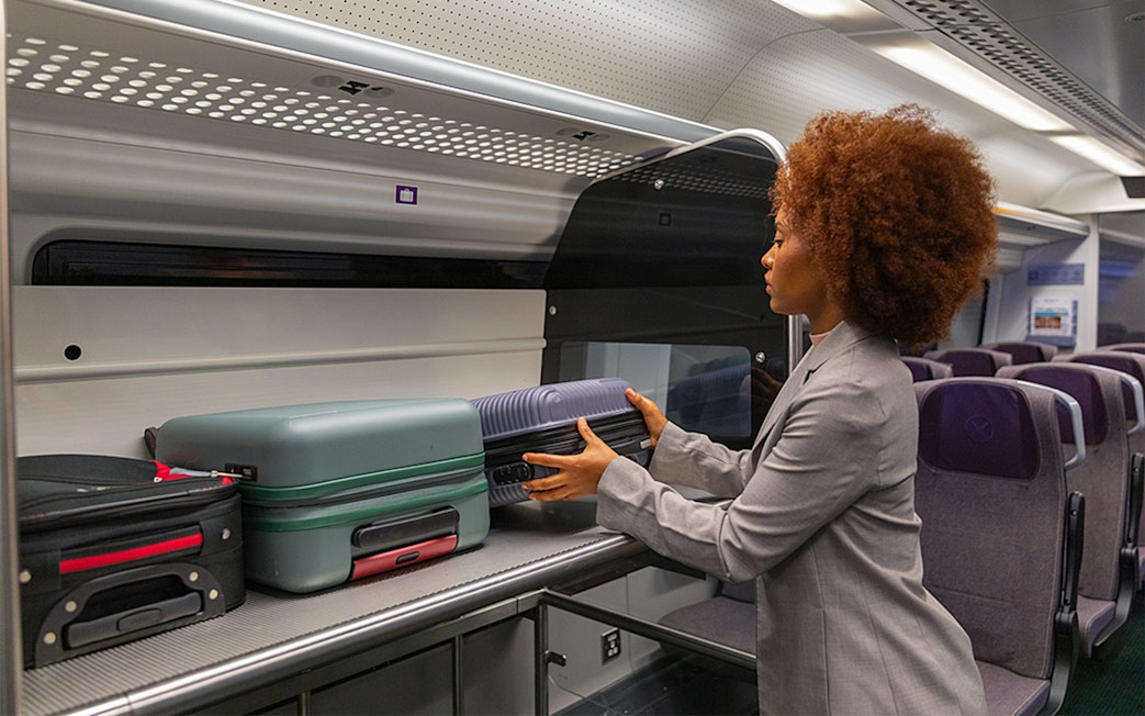 Passenger placing luggage in overhead compartment on Heathrow Express train to London Paddington.