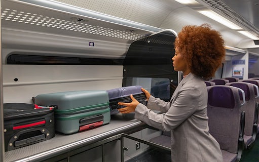 Passenger placing luggage in overhead compartment on Heathrow Express train to London Paddington.
