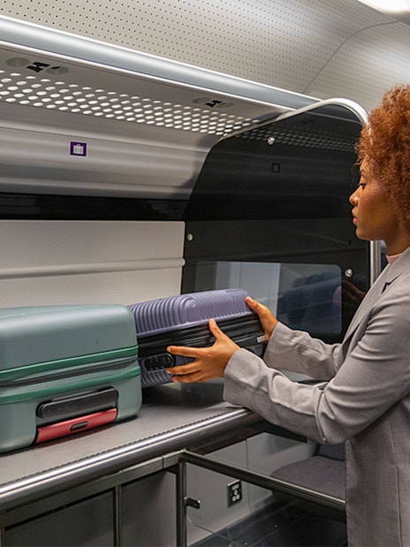 Passenger placing luggage in overhead compartment on Heathrow Express train to London Paddington.