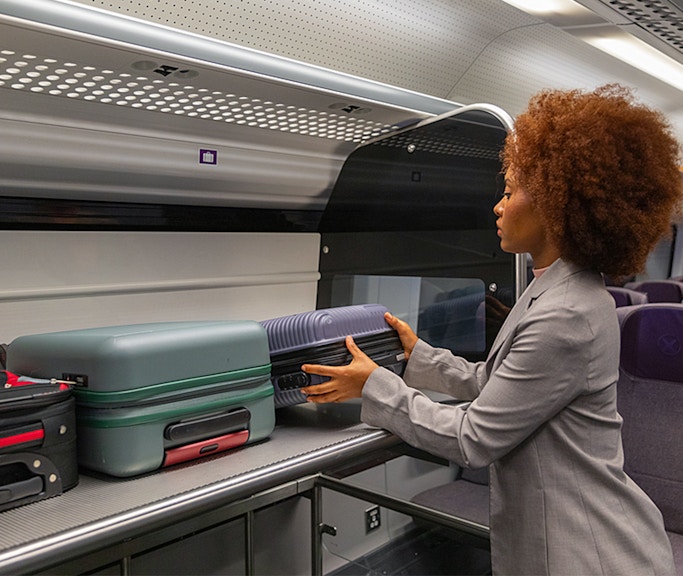 Passenger placing luggage in overhead compartment on Heathrow Express train to London Paddington.