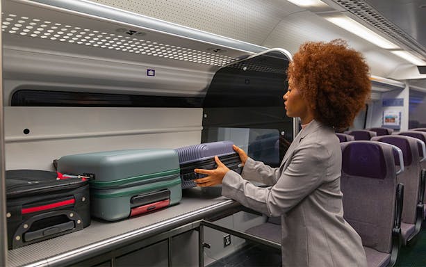 Passenger placing luggage in overhead compartment on Heathrow Express train to London Paddington.