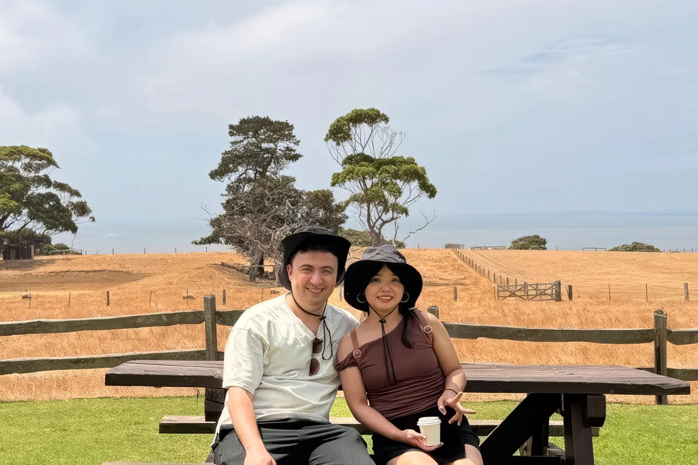 Couple sitting on a bench with a scenic view of Phillip Island's countryside in the background.
