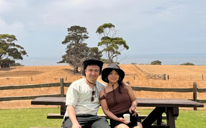 Couple sitting on a bench with a scenic view of Phillip Island's countryside in the background.