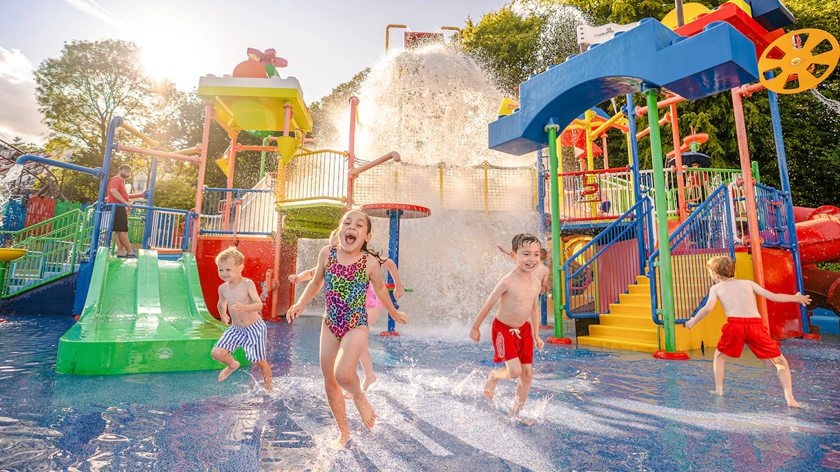 Children playing in the Splash Zone at Legoland Windsor with water slides and fountains.