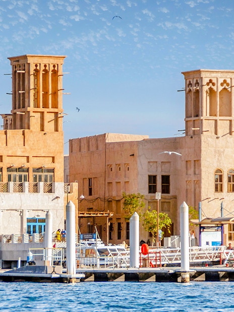 Traditional buildings along Dubai Creek with wind towers and waterfront view.
