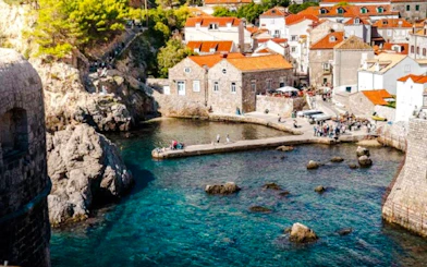 Aerial view of Dubrovnik old town harbor with stone buildings and clear blue water.