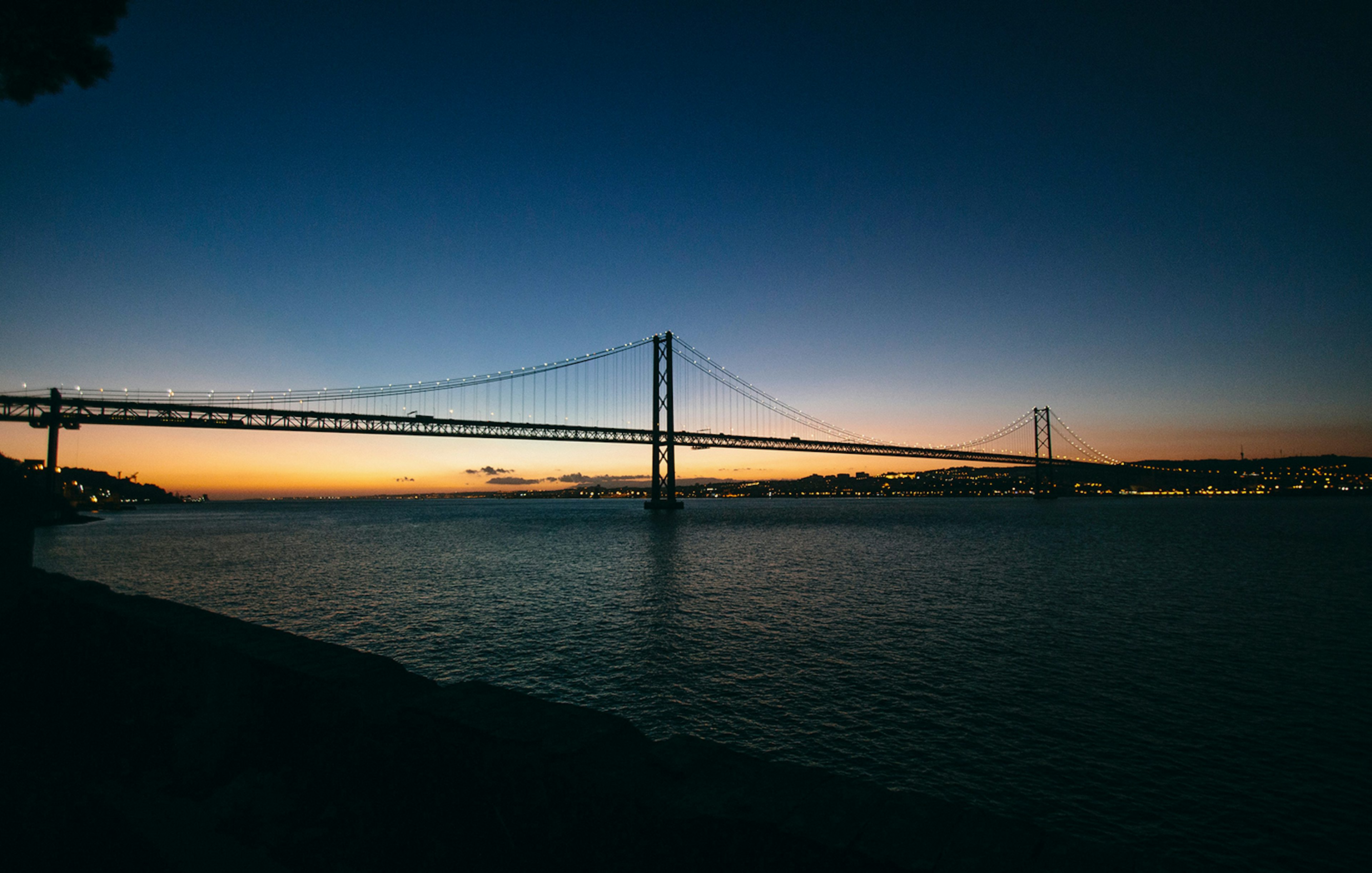 Lisbon's 25 de Abril Bridge illuminated at sunset during a night cruise.