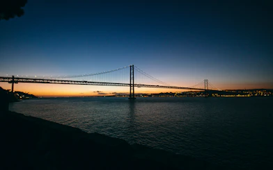 Lisbon's 25 de Abril Bridge illuminated at sunset during a night cruise.