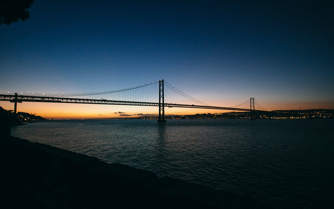 Lisbon's 25 de Abril Bridge illuminated at sunset during a night cruise.