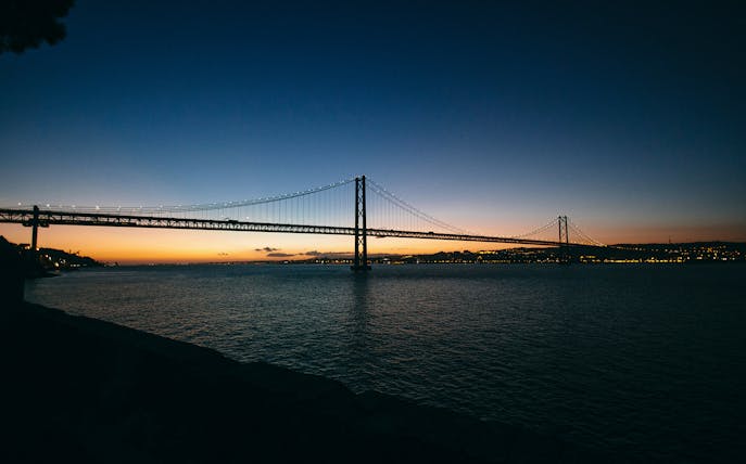 Lisbon's 25 de Abril Bridge illuminated at sunset during a night cruise.