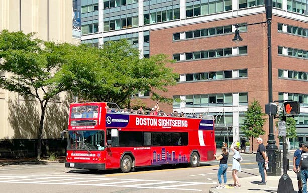 Sightseeing bus touring through downtown Boston with passengers on the upper deck.