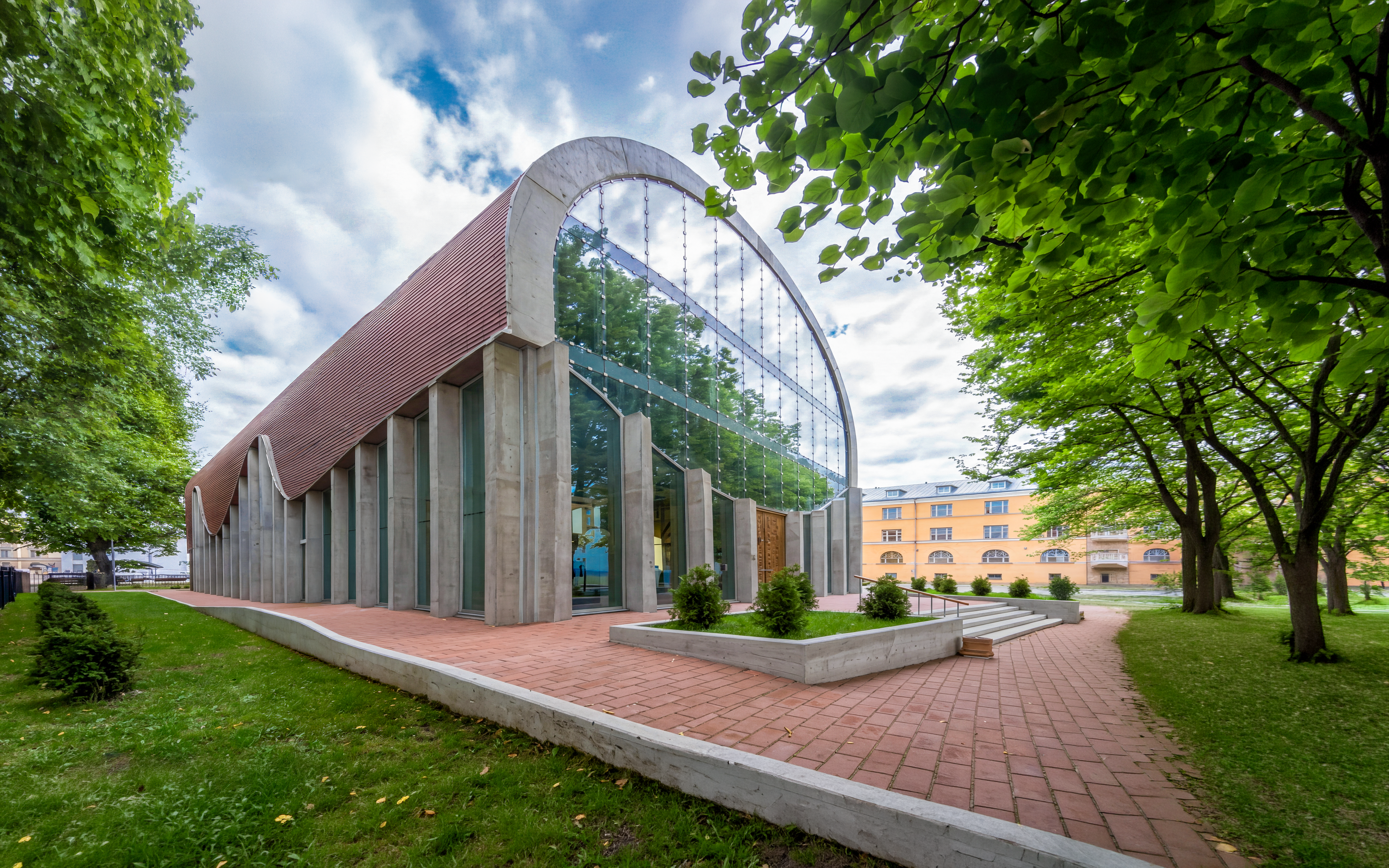 Tallinn Synagogue with modern glass facade and arched roof, surrounded by trees.
