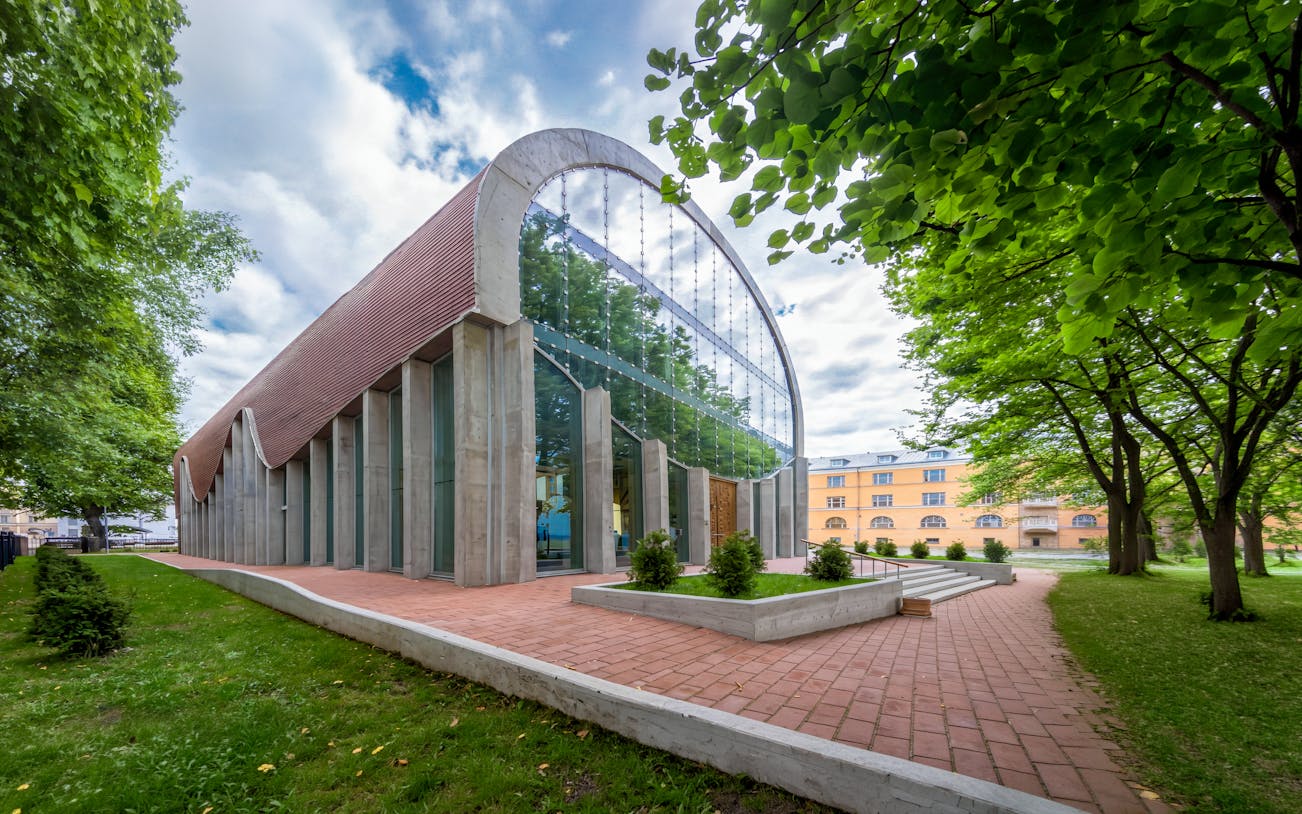 Tallinn Synagogue with modern glass facade and arched roof, surrounded by trees.
