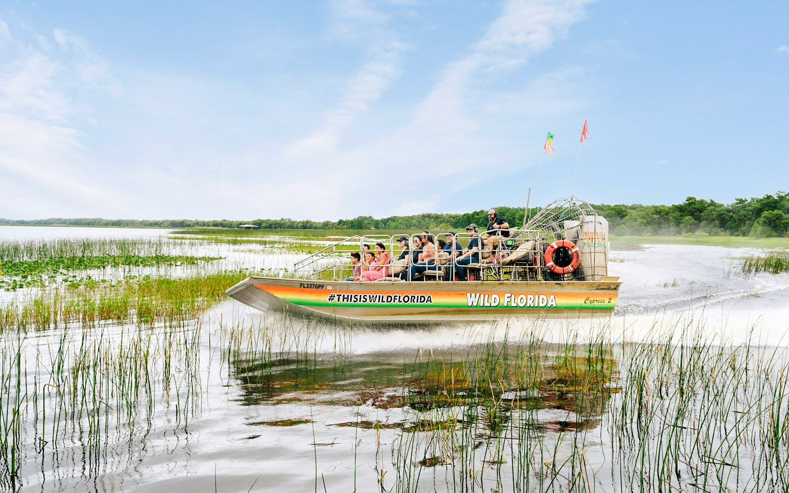 Guests on airboat touring Everglades, Florida, surrounded by wetlands.