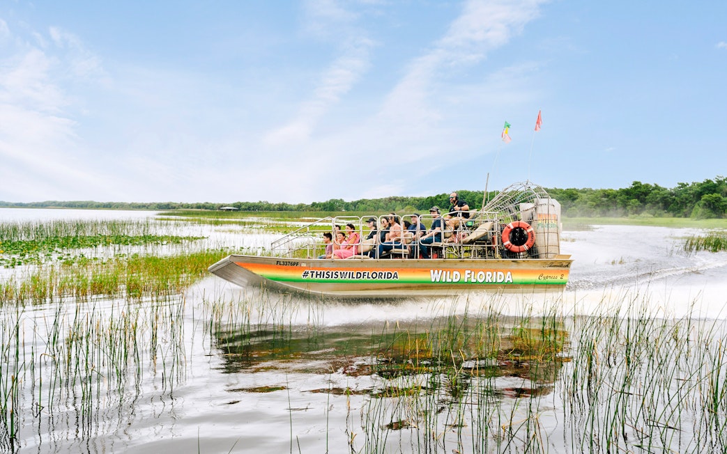 Guests on airboat touring Everglades, Florida, surrounded by wetlands.