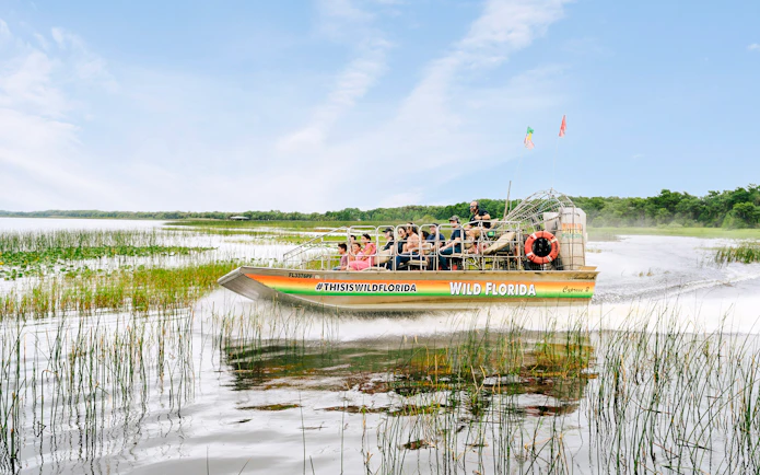 Guests on airboat touring Everglades, Florida, surrounded by wetlands.