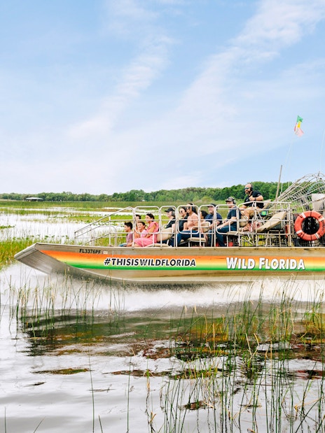 Guests on airboat touring Everglades, Florida, surrounded by wetlands.