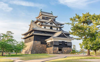 Matsue Castle in Shimane, Japan, surrounded by trees under a clear sky.