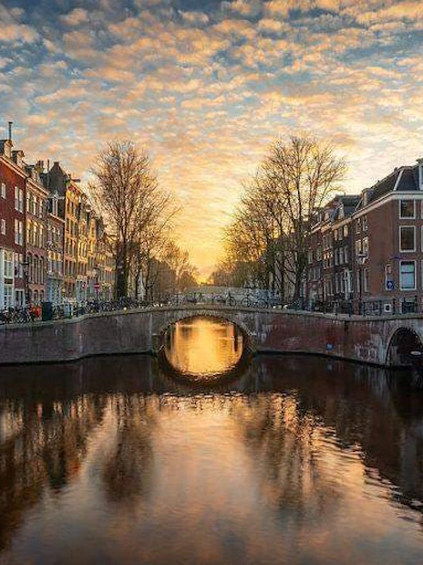 Amsterdam canal at sunset with historic buildings and bridge reflecting in the water.