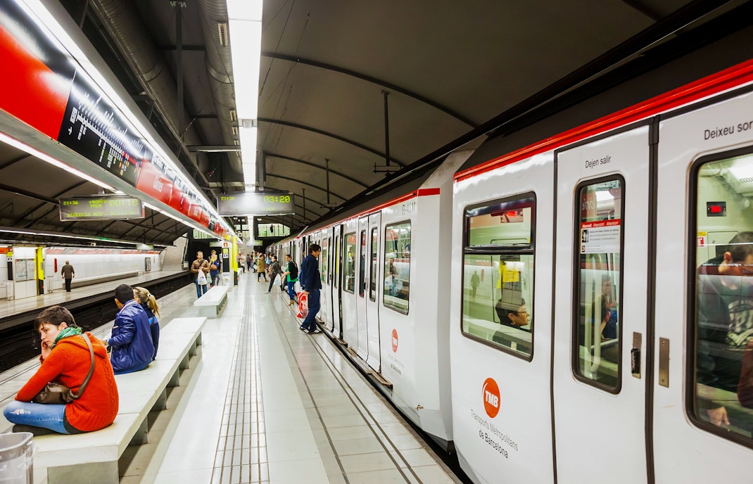 Barcelona Metro train arriving at a platform with passengers waiting in the station.