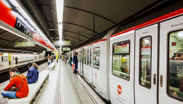 Barcelona Metro train arriving at a platform with passengers waiting in the station.